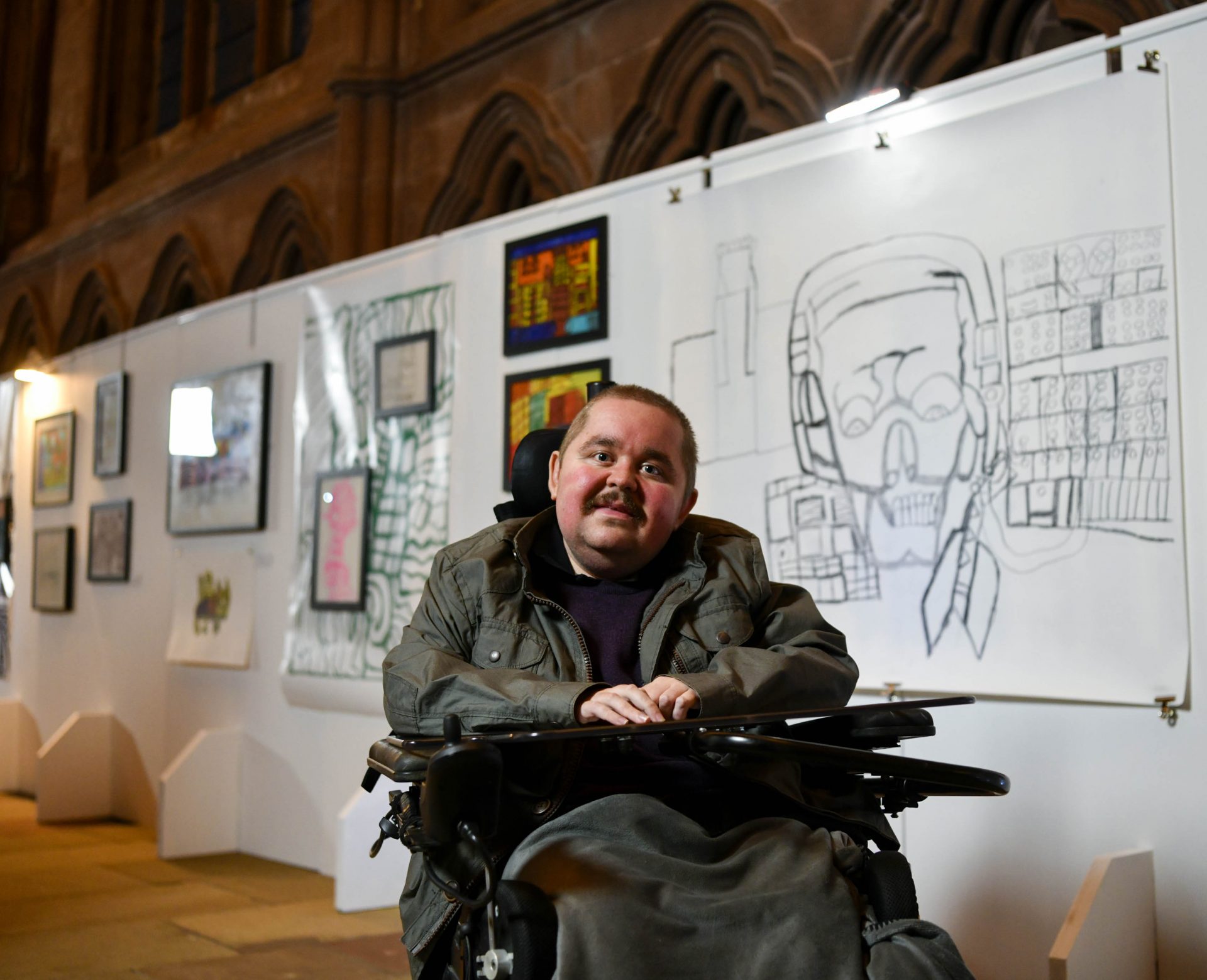 Artist Harvey Tye sitting in the middle of his exhibition in Carlisle Cathedral