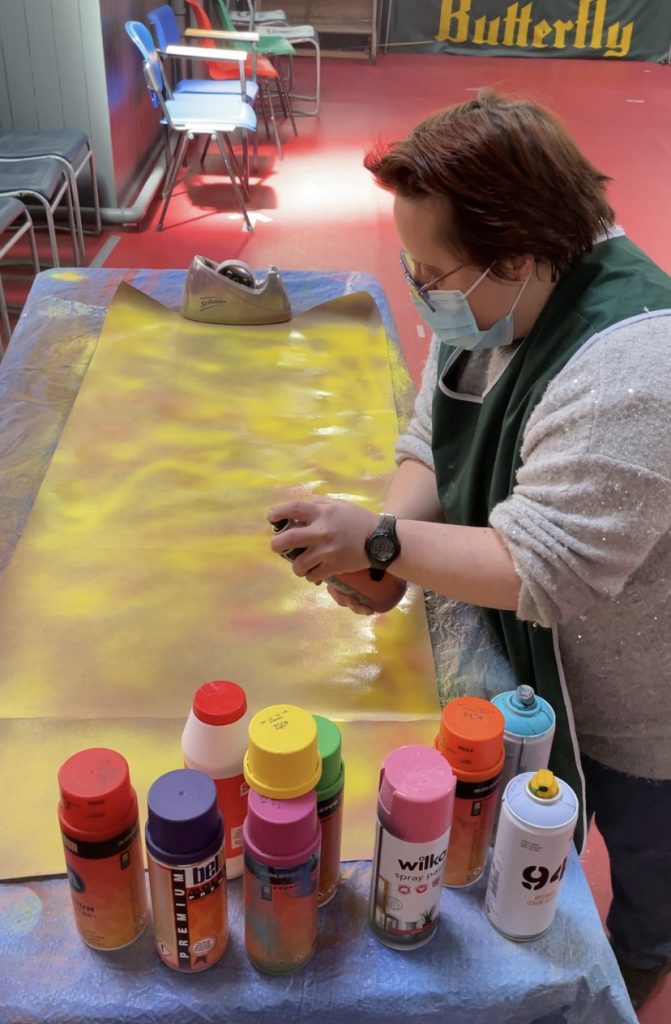 A lady spray painting on a large canvas