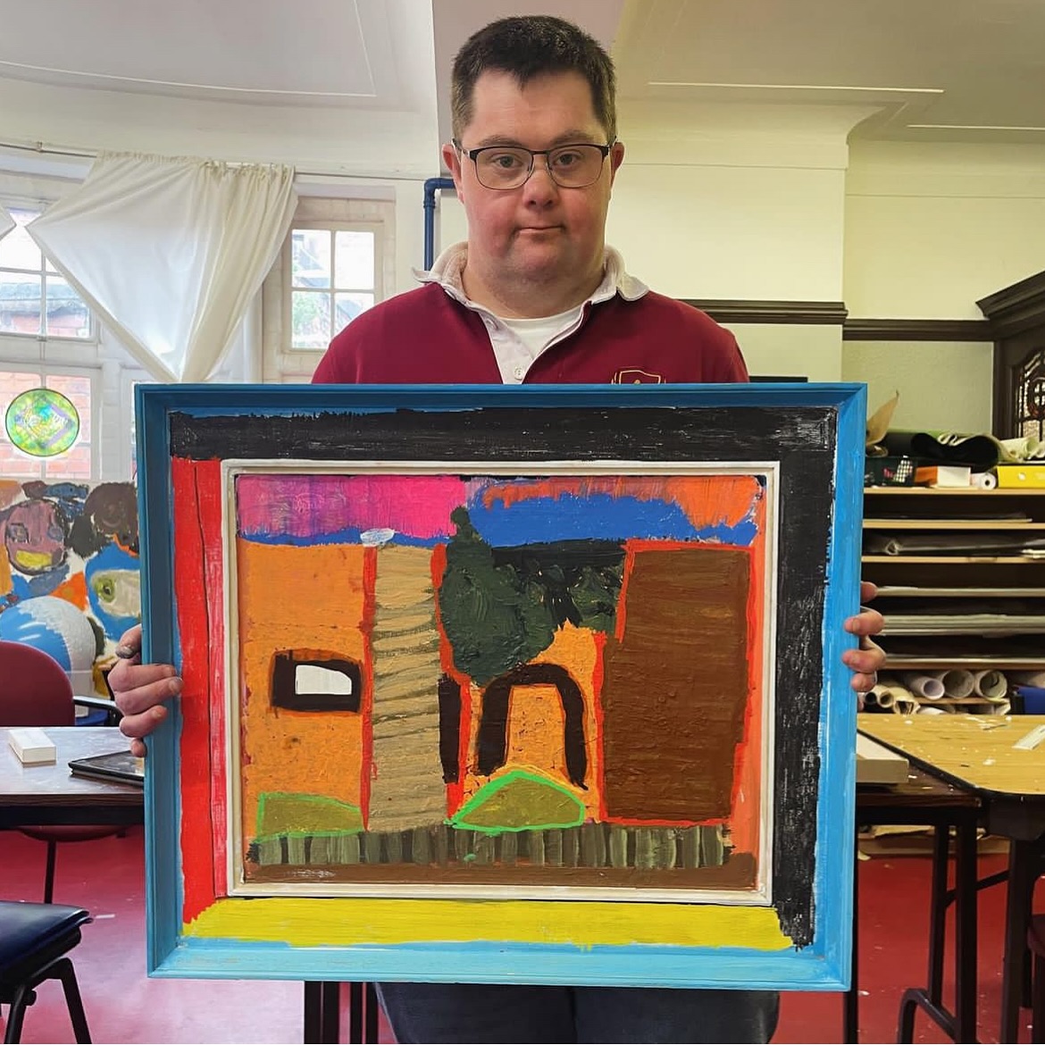 White man with dark hair and glasses holding a colourful, abstract landscape.