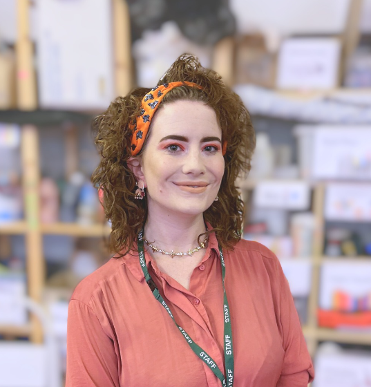 white woman, pink blouse. smiley face. brunette, curly hair and orange headband. pink eye makeup.