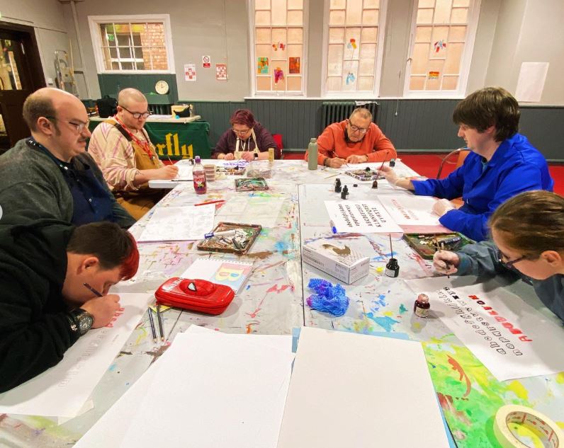 Six artists gathered around a table and working in a focused manner on a creative project